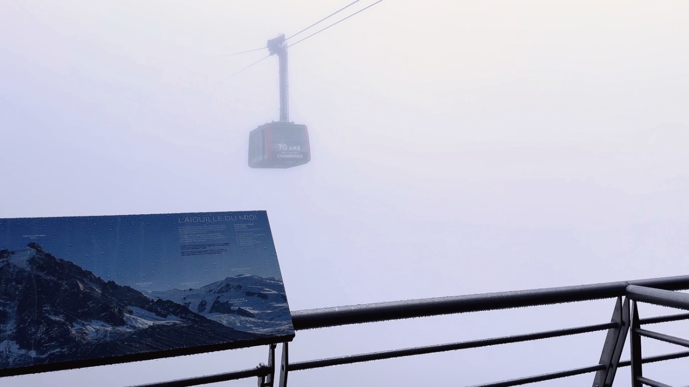 A cable car emerging from thick mist on the mountainside