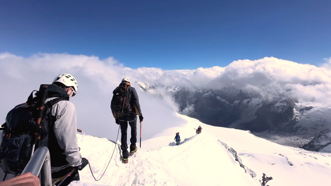 Fully kitted climbers on a snow ridge above the clouds