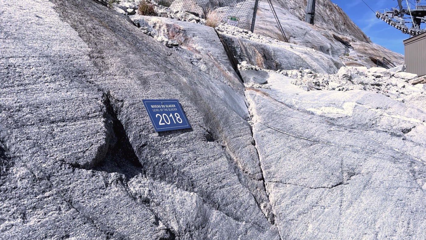 A blue sign on bare granite reading 'Level of the glacier 2018'