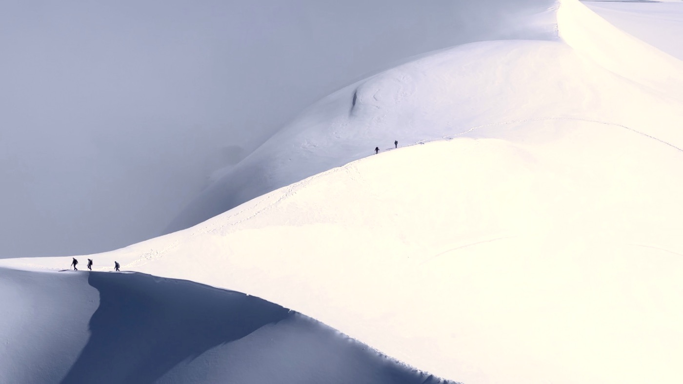 Tiny climbers crossing a vast white snowfield