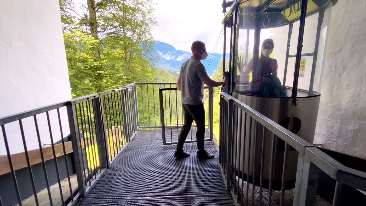 A staff member on a platform beside the small round private funicular cabin