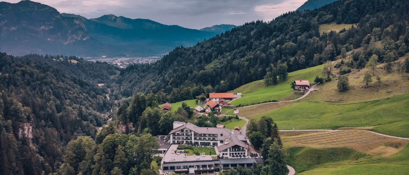 An aerial view of the Das Graseck wellness hotel perched on a forested alpine slope above the valley