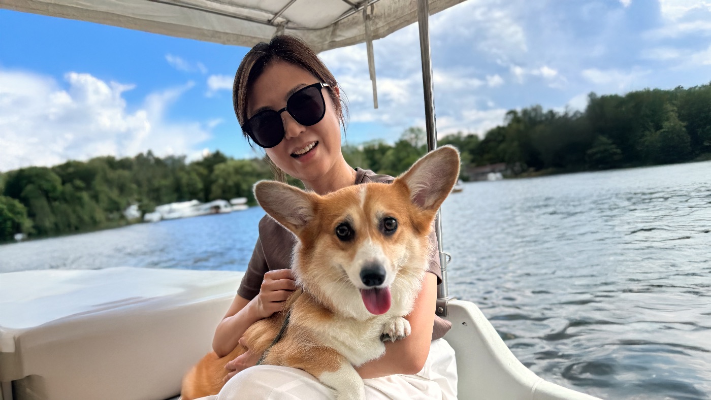 A woman in sunglasses holding Scottie the corgi on a boat on a lake in Karuizawa