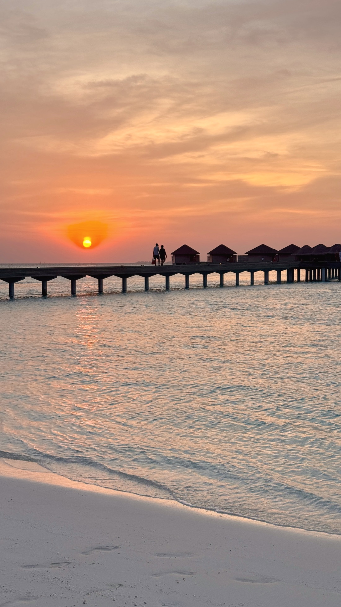 A couple walking the pier into a Maldives sunset