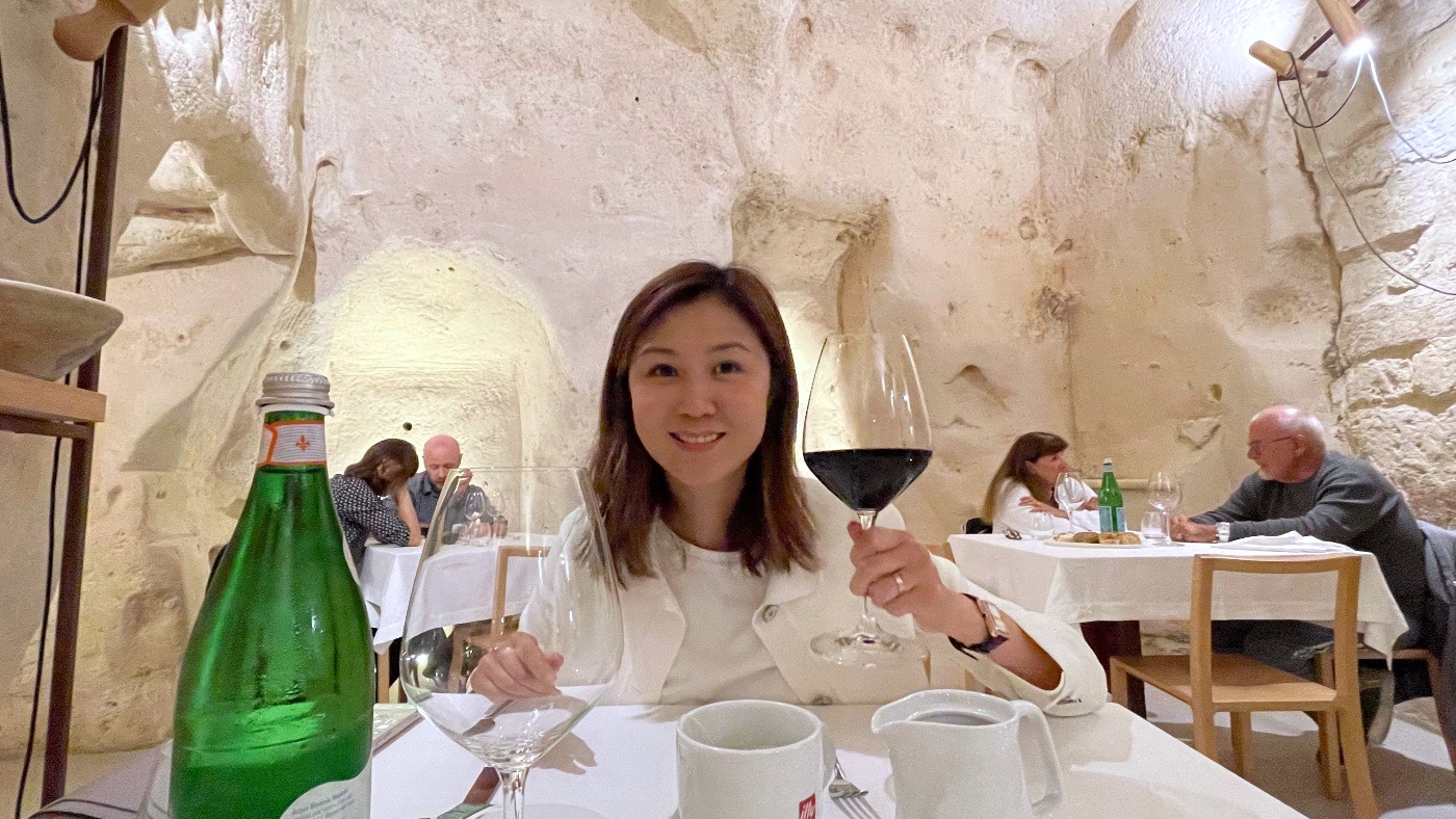 A woman raising a glass of red wine at a table in a cave restaurant in Matera