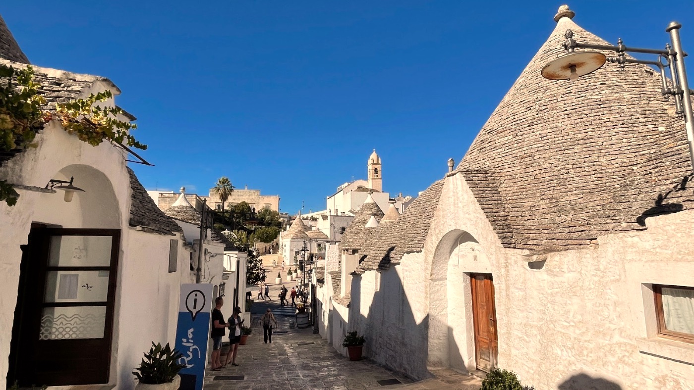 The cone-roofed white trulli houses lining a sunlit lane in Alberobello