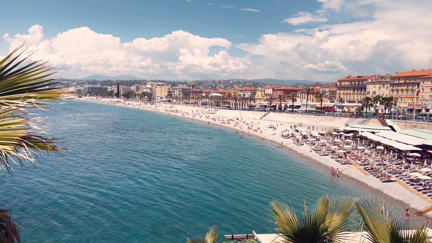 The Baie des Anges in Nice — turquoise sea, the pebble beach and old town backed by distant hills