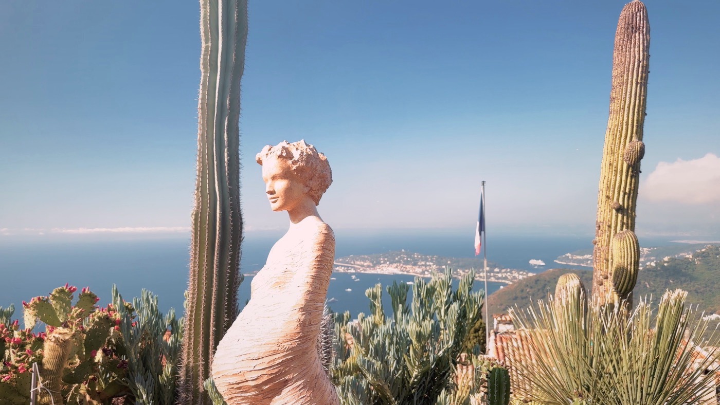 A pale statue among tall cacti at the Exotic Garden, the sea far below