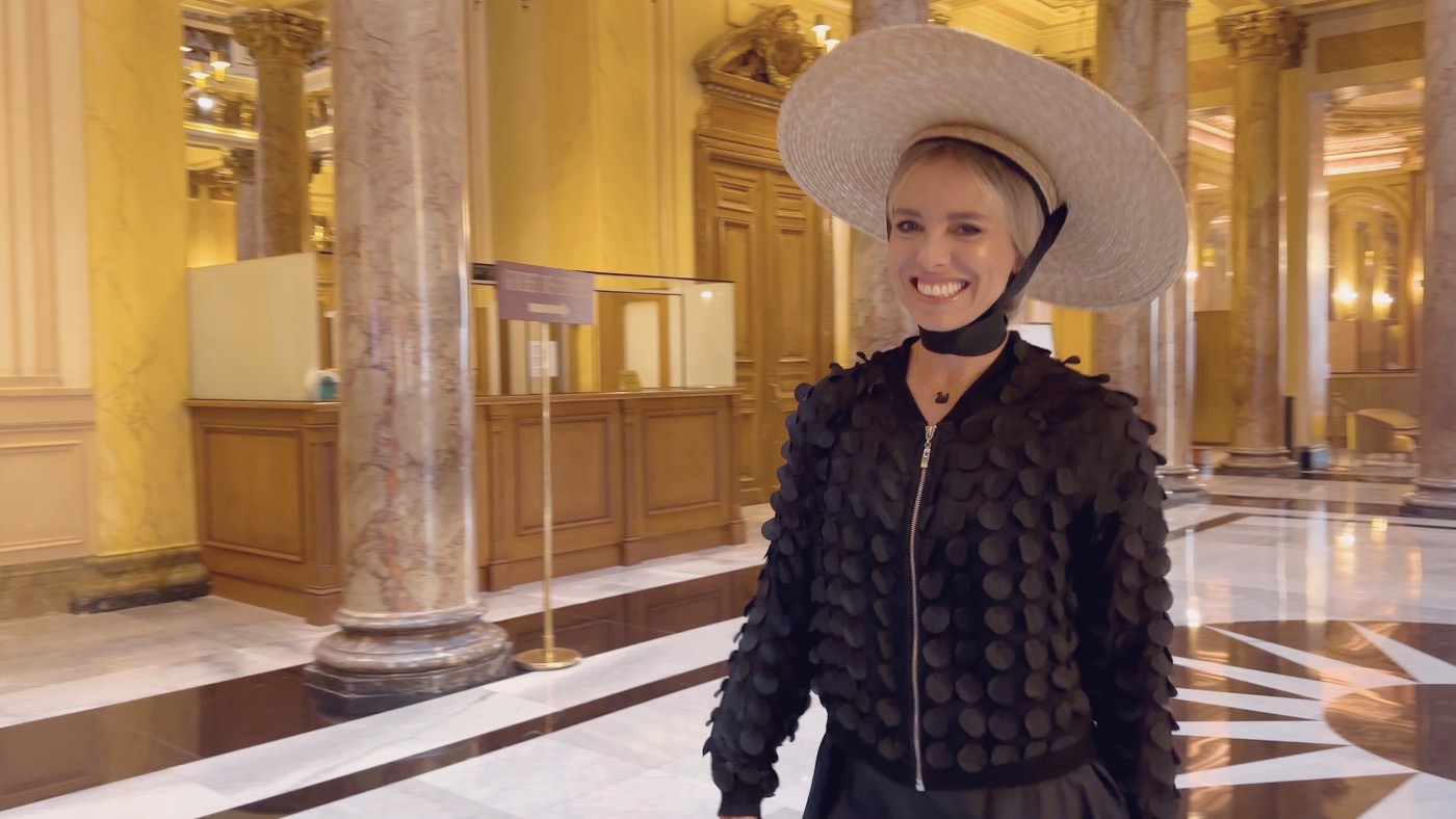 A woman in an elegant black outfit and wide-brimmed hat smiling in the casino’s marble hall
