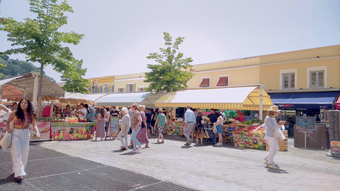 An open-air market in Nice with striped awnings, fruit stalls and strolling shoppers